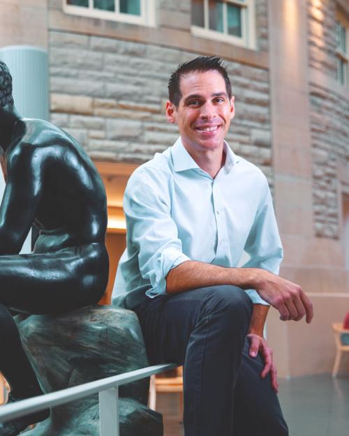 Person smiling next to a sculpture of a person sitting