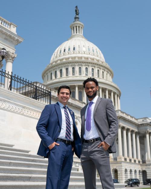 		Two people in suits standing in front of the recognizable white dome of the US Capitol Building
	