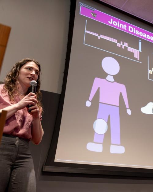 Person holding a microphone near a large screen projecting a slide about "Joint disease across the species"
