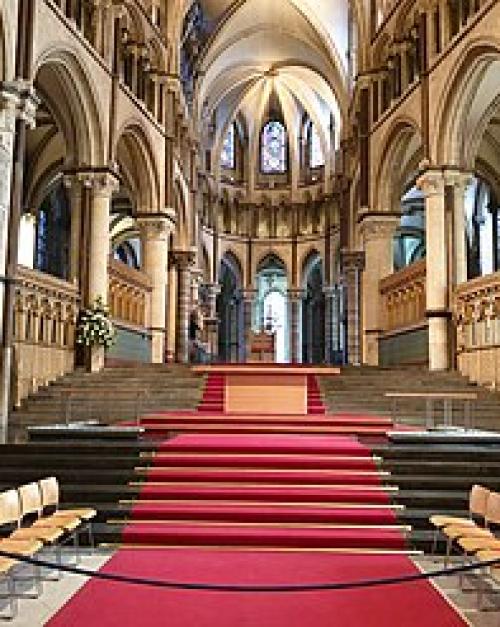 Columns and arches form the walls, with a red carpet leading up to the alter in this image of the interior of the cathedral 