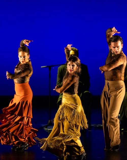 People on a stage, dancing dramatically in yellow and orange costumes