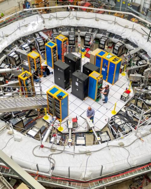 Very large, while ring – a physics experiment setup – dwarfs equipment in its center and people working in it 