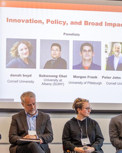 Five people on a stage with a screen behind them