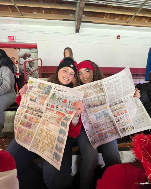 two people holding newspaper at a hockey game