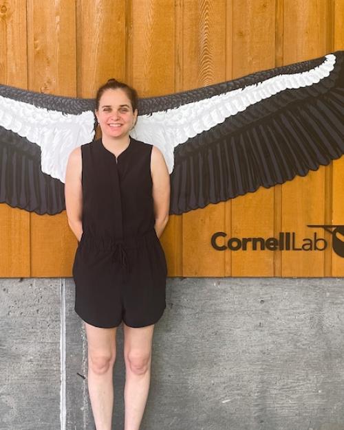 Person in a black outfit standing so a very large pair of black and white wings – a lifesize model of a California condor – spreads out behind her. It looks like she has wings