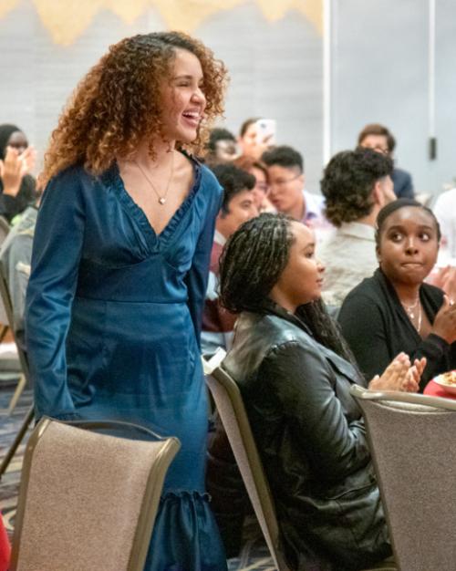 Person walking past a table where others sit, looking on and applauding