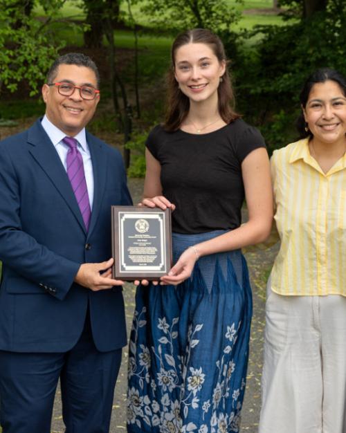 Five people lined up for a photo: in the center a college student award recipient holds a plaque