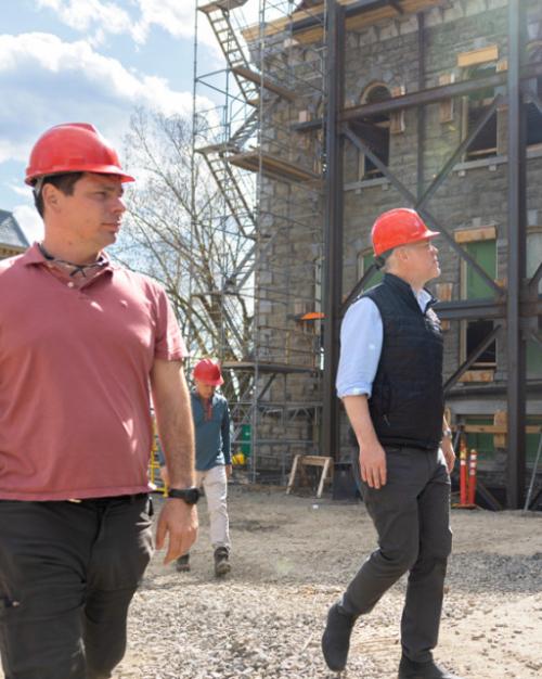 Two people in red hard hats walk through a building construction site