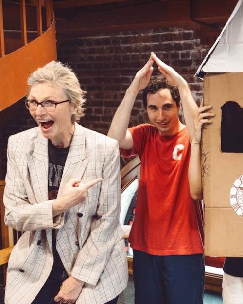 Four people goofing off in a brick-walled room. One wears a cardboard clock tower costume