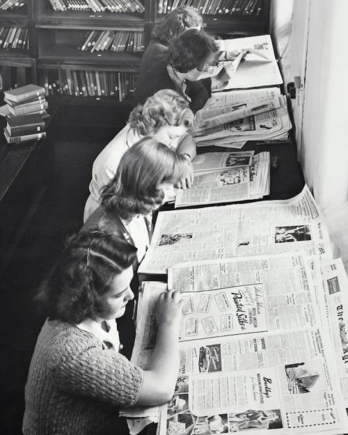 Historic black and white image of five people reading newspapers together at a table