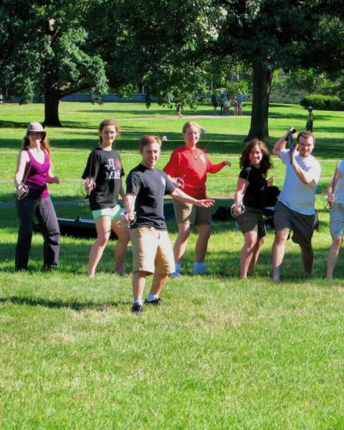 Several people pose imposingly with swords on the green lawn of Cornell's Arts Quad