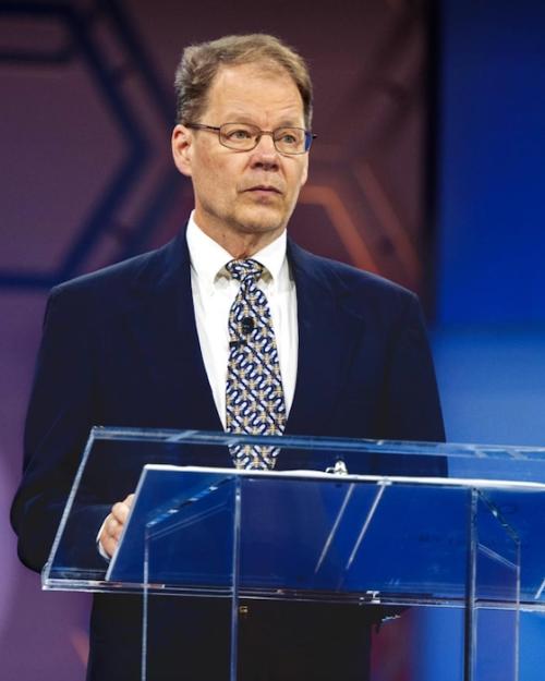 Person standing at a podium, looking serious
