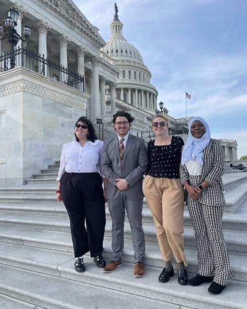 Four people stand on stone steps withe the dome of the U.S. Capitol building in the background