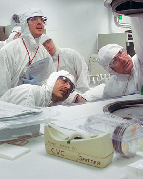  People in white protective gear and goggles, in a lab