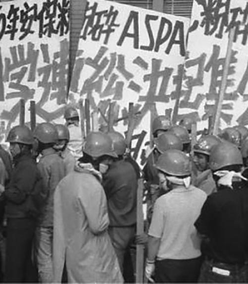  Japanese with helmets on in front of a  protest sign in Japanese