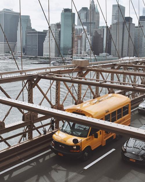 Yellow bus on a bridge, New York City in the background