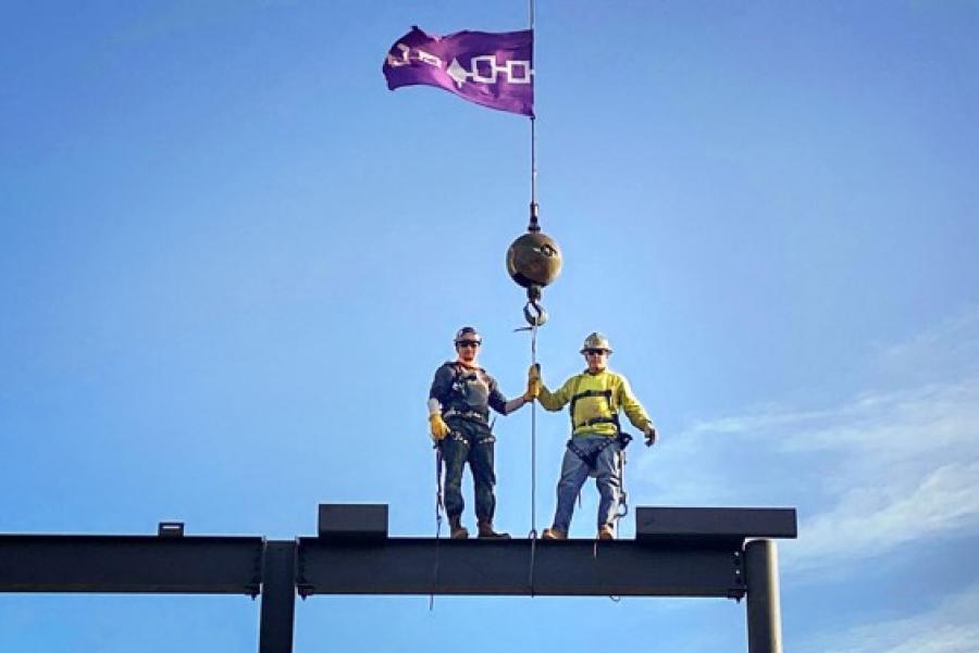 Two people in work hats, atop a building under construction