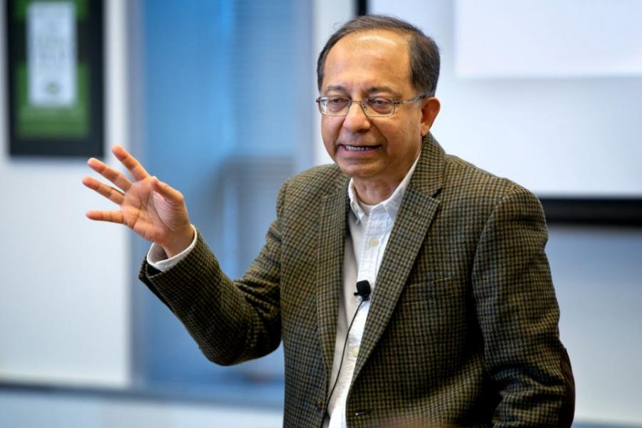 Kaushik Basu wearing a tweed jacket with hand upraised as he delivers a talk.