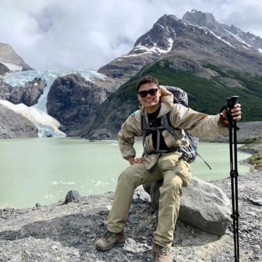 Ngoc Truong sitting on a rock in front of a lake and a mountain with glacier