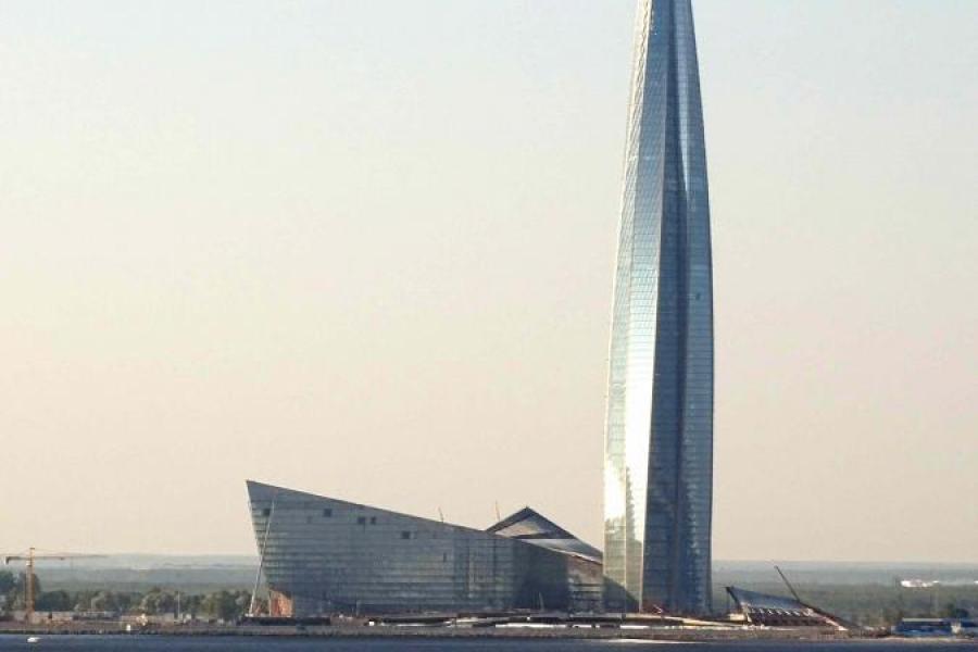 A rocketship-shaped skyscraper next to a building shaped like the prow of a ship, both steel-colored.