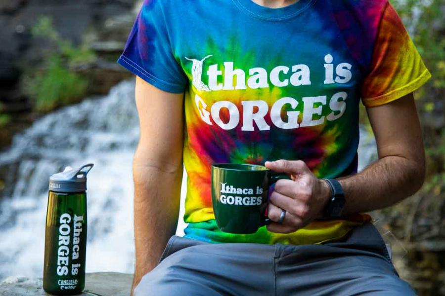 a person wearing an Ithaca is Gorges tshirt with mug and water bottle