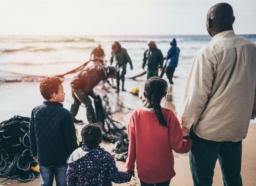 Man with children watching others pulling nets in from the sea