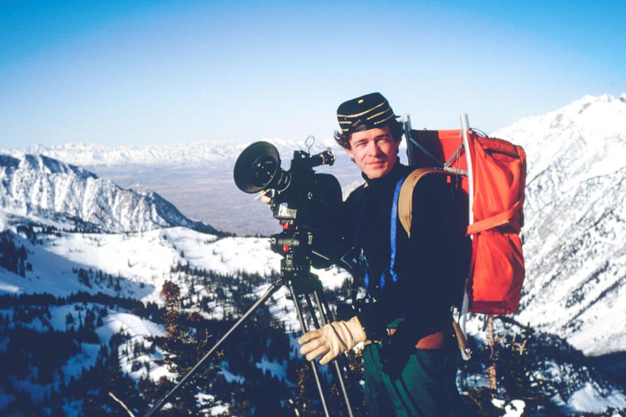 Person in hiking gear with a large camera; mountains in background