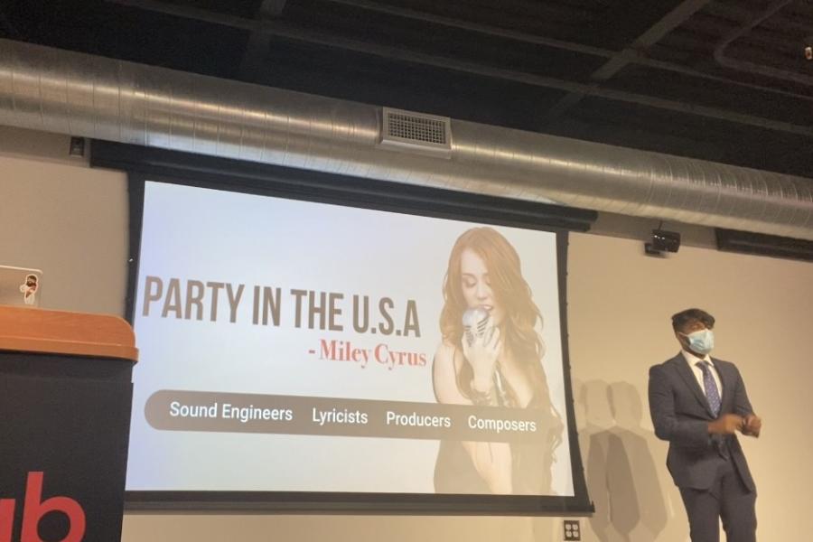 Two people on a stage with a large screen showing a singer