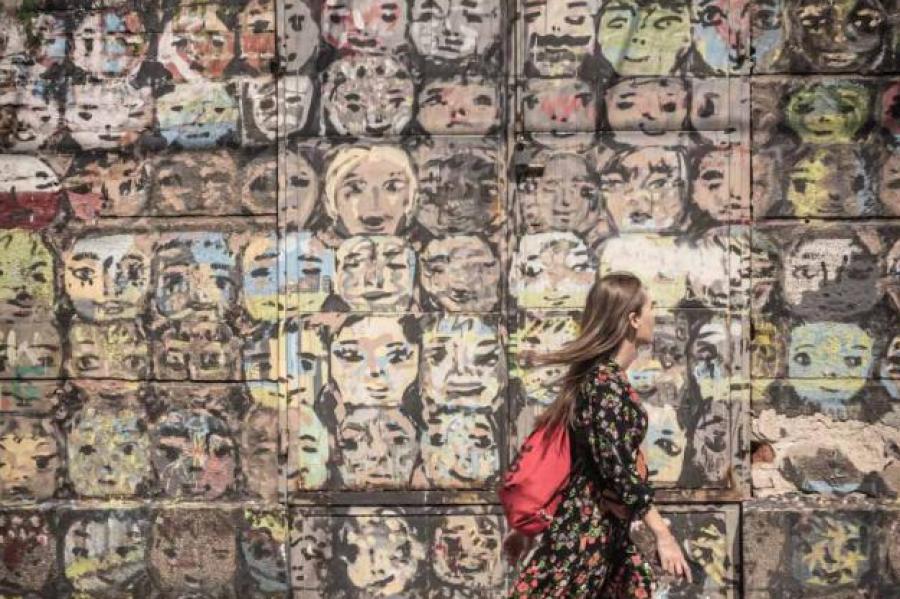 Person walking past a wall painted with many faces