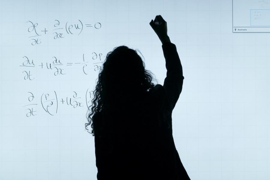 Person silhouetted against a white background, writing equations on a board