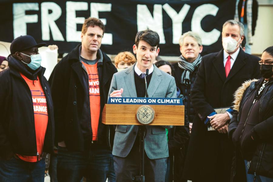 Person wearing gray suit speaks at a podium that says 'NYC LEADING ON CLIMATE'
