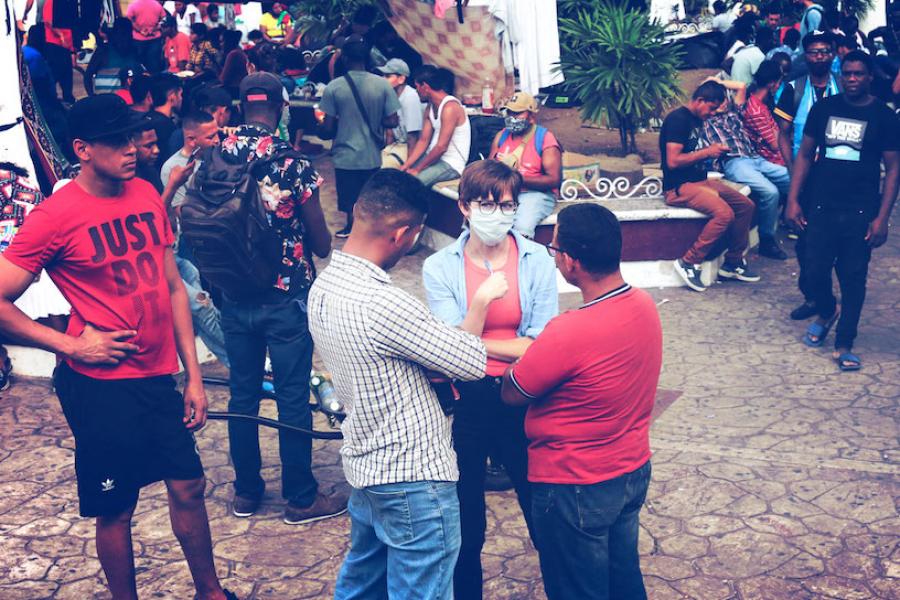 Crowd of people in a stone-floored courtyard; one person listens in the middle