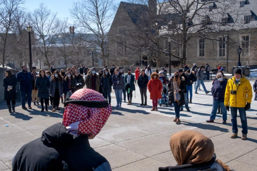 People stand in a half circle in a sunny outdoor plaza