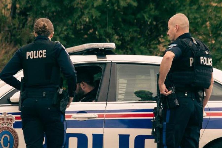 Two police officers stand near a police car
