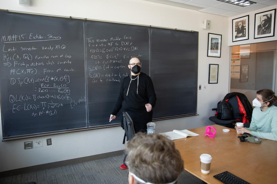 Person standing in front of a chalk board that is covered in mathematics notes