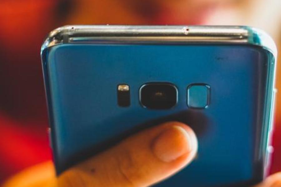 Hand holding a smart phone; face blurred in background