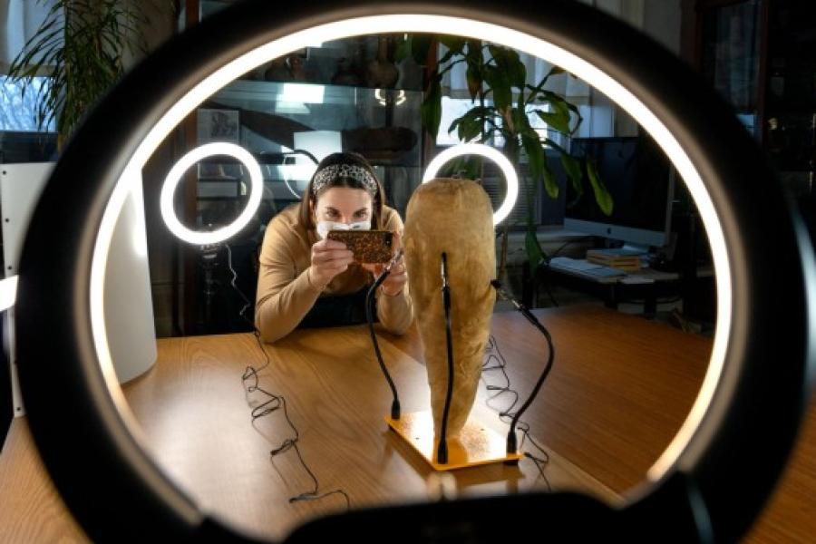 Person aims a camera at a tan artifact lit by circular white lights