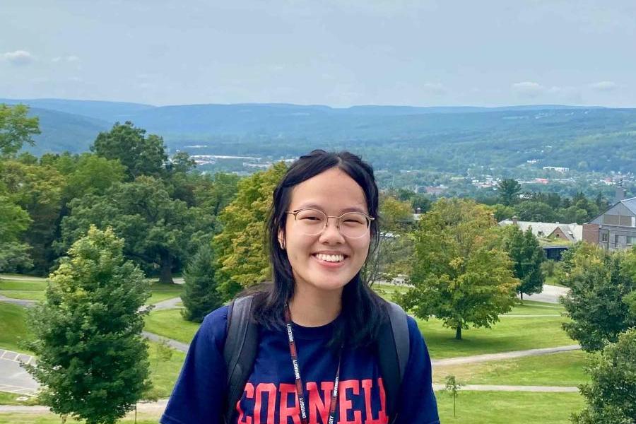 Eunice Ngai in a blue Cornell t-shirt with trees and the Ithaca hills in the background.
