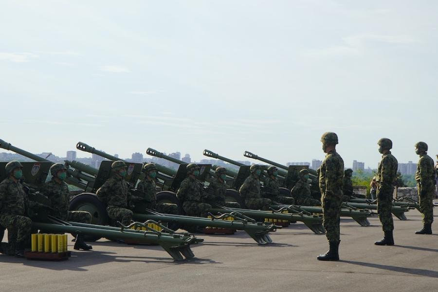 Solders stand at attention behind a row of heavy guns