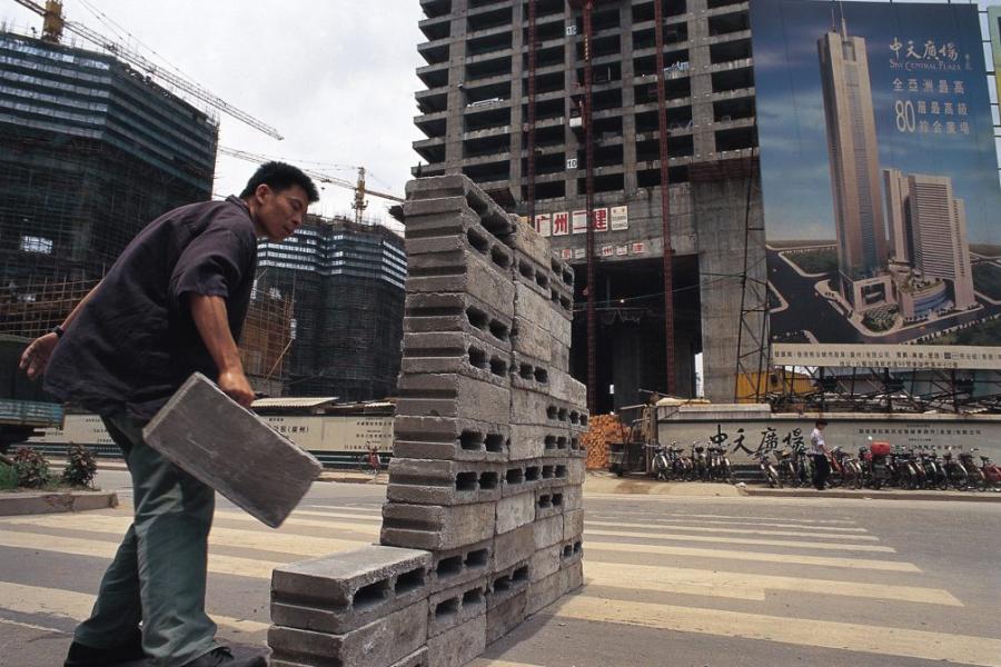 Person carries a heavy cement block around a wall