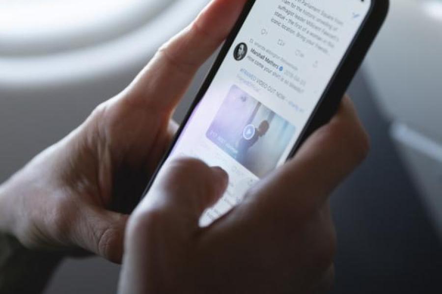 Two hands holding a cellphone and scrolling through a Twitter feed.