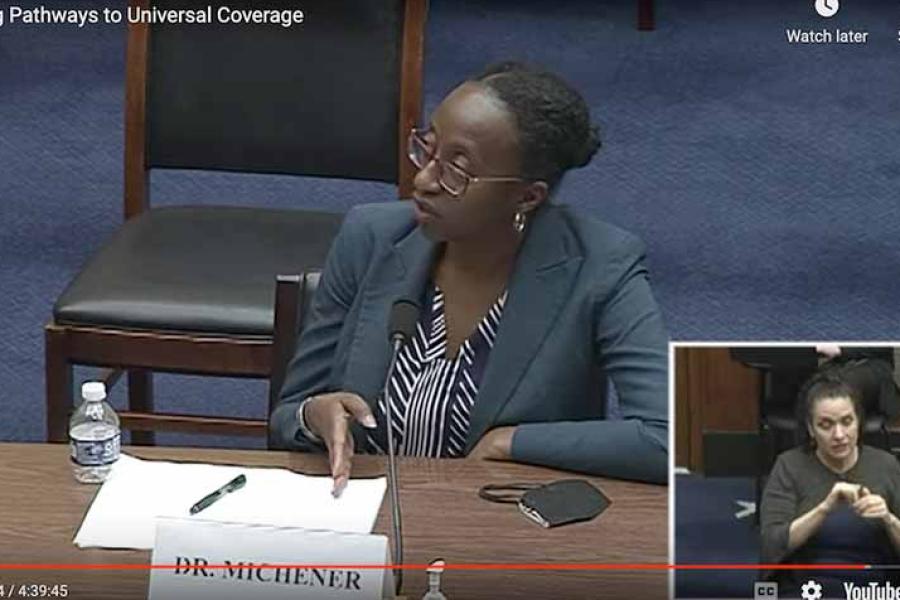 Person speaking in front of a microphone, seated at a wooden table