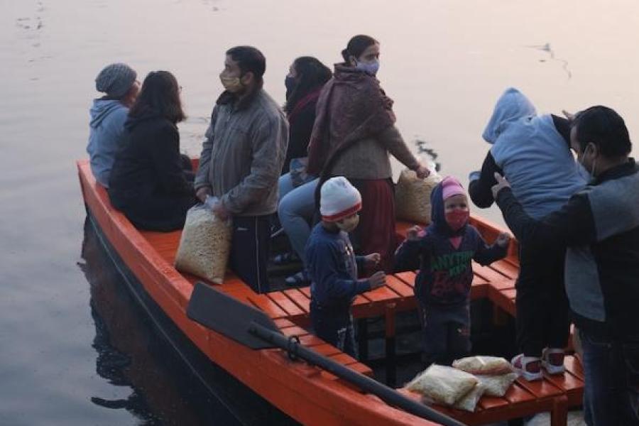 Sevearl people, including children, in a row boat with belongings. Birds fly overhead