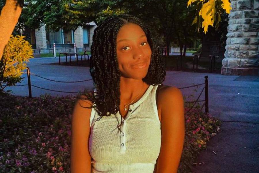 Valerie Odonkor in jean shorts and a sleeveless shirt under a tree outside Uris Library