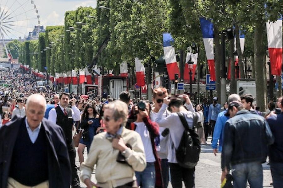 Thousands of people stroll up a wide avenue lined with red, white and blue flags