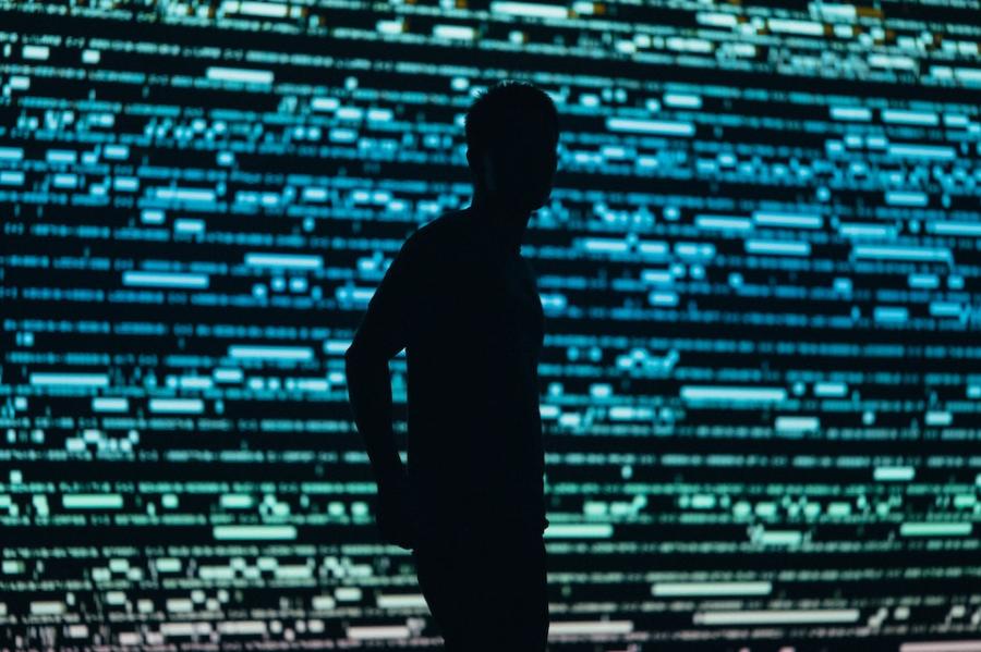 person silhouetted against a backgrond of green and blue lights