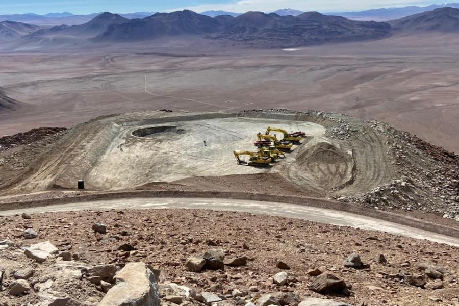 Flat ground and four construction vehicles; mountians in background