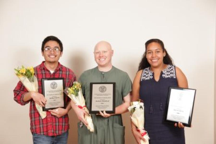 A dark-skinned man, bald White woman and African-American woman holding bouquets of flowers and their award certificates
