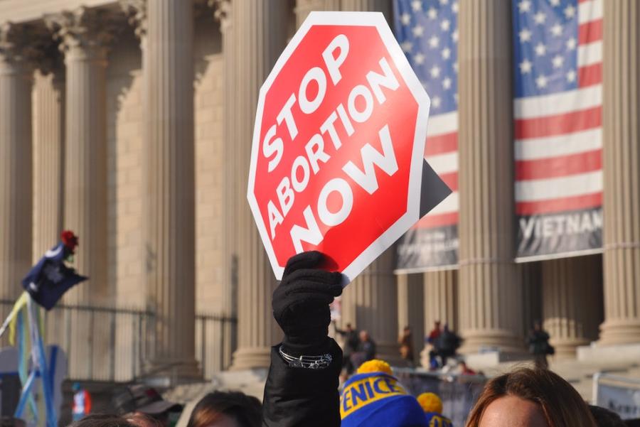 Red protest sign held up outside a stone-columned building