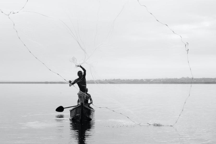 Person casts a net from a canoe on a calm lake